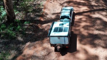 Off-grid solar camper with solar panels and vehicle on dirt road.