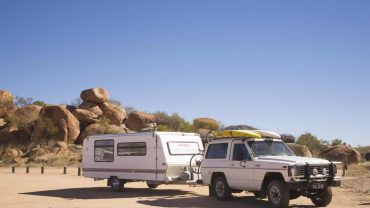 Caravan and 4WD vehicle parked in a desert landscape with rocks and clear blue sky.