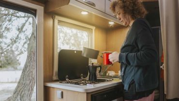 Woman pouring coffee in a compact RV kitchen with natural light.