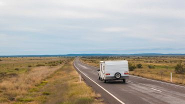 A campervan driving along a remote open road in the Australian outback.
