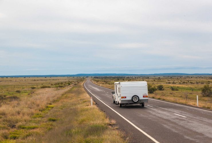 A campervan driving along a remote open road in the Australian outback.