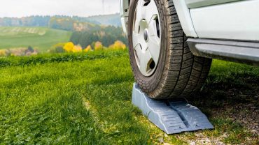 Car on wheel chock in a lush green field with rolling hills in the background, emphasizing safety an.