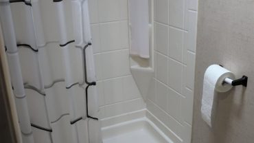 Shower stall with white tiles and a towel on a rack in a compact bathroom.