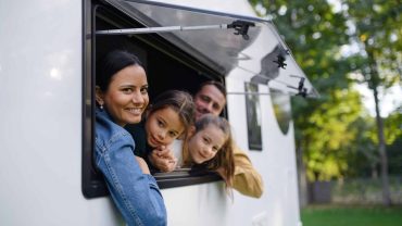 Family enjoying time at a caravan window in a scenic outdoor setting.