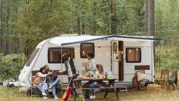Camping with family in forested area with caravan and outdoor setup.