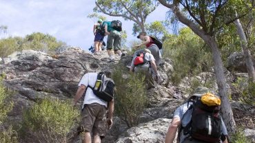 Hiking group climbing rocky trail with backpacks in natural outdoor setting.