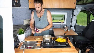 Man cooking breakfast in a compact campervan kitchen with stove and utensils.