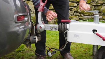Towing and camping equipment setup with a vehicle and trailer hitch in outdoor setting.