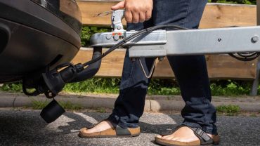 Person attaching a trailer to a vehicle with a tow hitch outdoors.
