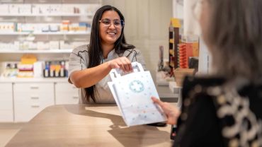Woman handing over a shopping bag at a pharmacy counter.