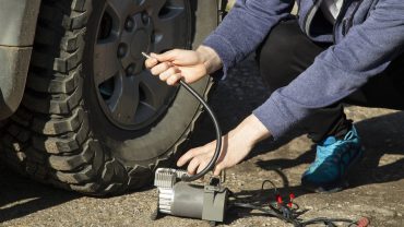 Person inflating an off-road vehicle tire using a portable air compressor.