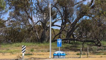 Rest area with shade trees, sign, and picnic table in a rural setting.