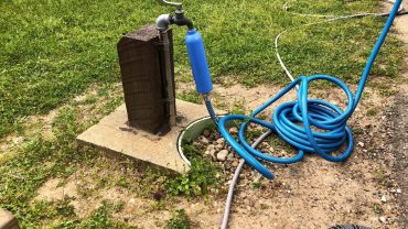 Water hose connected to outdoor tap on grass.