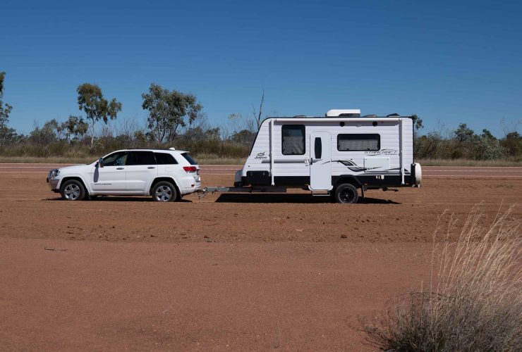 Caravan and car parked on a dirt road in the Australian outback under a clear blue sky.