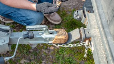Close-up of a person connecting a trailer hitch to a caravan in a camping setup.