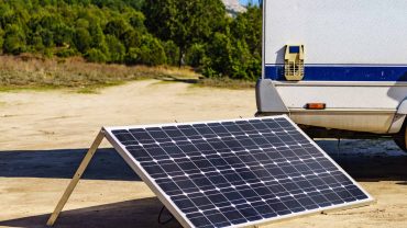 Solar panel on a portable stand near a campervan in a scenic outdoor setting.