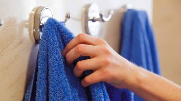Hand hanging blue towel on bathroom hook, close-up.