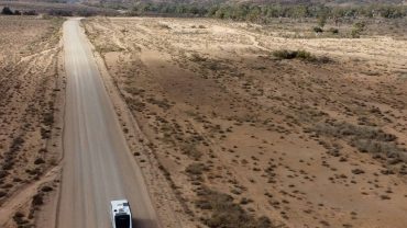 Long dirt road through arid Australian outback landscape with two vehicles.