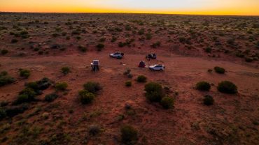 Sunset over desert campsite with vehicles and tents in Australia, showcasing outdoor adventure and c.