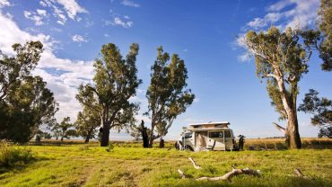 Australian RV parked in a scenic rural landscape with trees and blue sky.