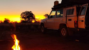 Camping van with campfire at sunset in the Australian outback.