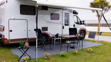 Modern RV camping setup with outdoor table, chairs, and shade in a grassy area.