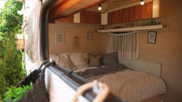 Interior view of a cozy camper bedroom with bed, pillows, and wooden accents.