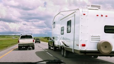Road trip scene with campervan and vehicles on open highway under cloudy sky.