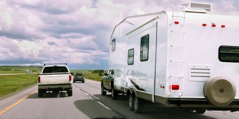 Road trip scene with campervan and vehicles on open highway under cloudy sky.