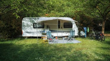 Caravan with outdoor seating and bicycles in a lush green park.