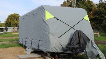 Outdoor camping caravan with protective cover and gear setup.