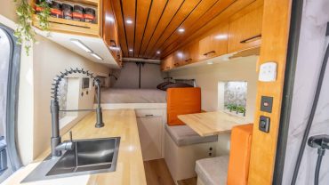 Compact campervan interior with kitchen, seating, and sleeping area.