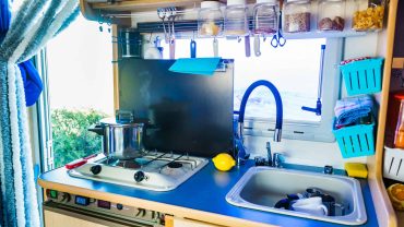 Compact campervan kitchen with stove, sink, and organized storage jars.