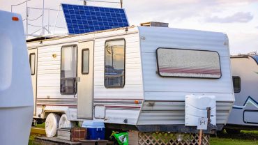 Vintage caravan with solar panels, outdoor storage, and scenic background.