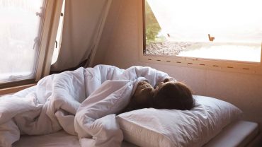 Traveling Big Lap Bible campervan interior with sleeping person, cozy bed, and scenic window view.