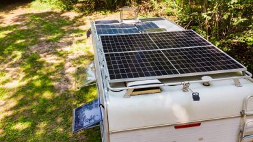 Solar panels installed on campervan roof in a lush forest setting.