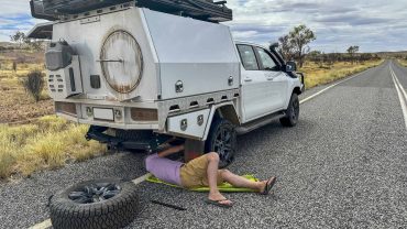 Caravan repair scene with a person fixing a camper trailer on a remote road.