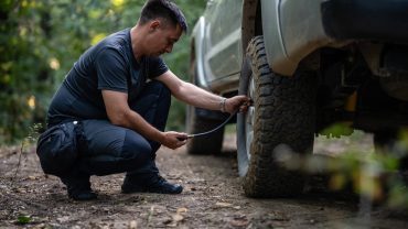 Man inspecting vehicle tire on rugged trail.
