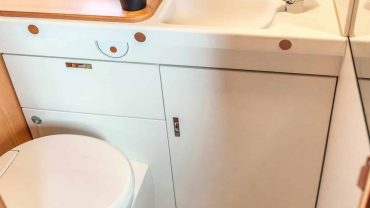 RV bathroom with sink, toilet, and wooden mat, perfect for travel and camping adventures.