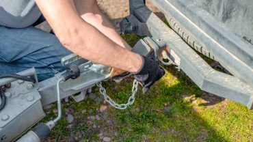 Person attaching trailer hitch to a caravan with a chain and tools.