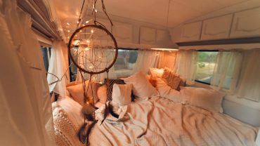 Interior of a cozy camper van with a bed, dreamcatcher, and warm lighting.