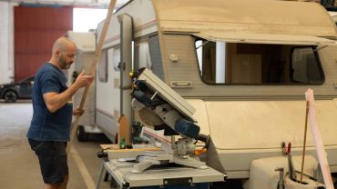 Man working on campervan renovation with saw and wood in workshop.