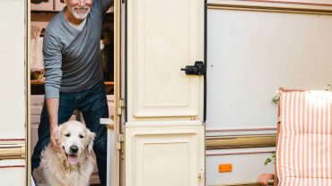 Man and golden retriever at the entrance of a caravan during camping.