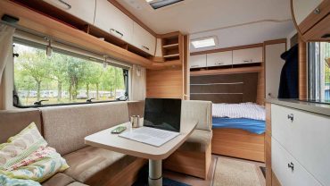 Compact camper interior with a cozy lounge, bed, and large windows for natural light. Perfect for tr.