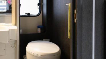 Small RV bathroom with toilet, window, and storage cabinet.