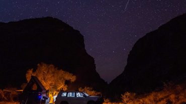 Night sky with stars and a shooting star over a vehicle and camper at Big Lap Bible campsite.