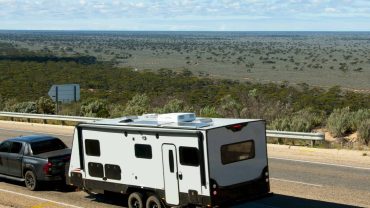 RV traveling on a remote Australian highway with open landscape and blue sky.