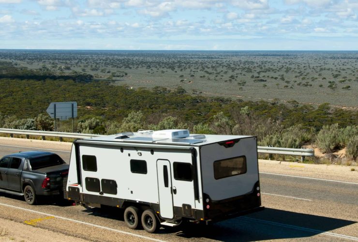 RV traveling on a remote Australian highway with open landscape and blue sky.