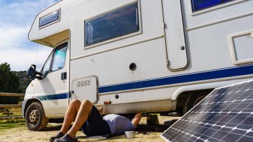Motorhome repair scene with person working underneath a campervan, solar panel nearby.