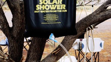 Portable solar shower bag hanging on a tree in outdoor setting.